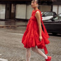 Guest wears red asymmetric dress, white laced tights and red sneakers outside The Cecilie Bahnsen show during Womenswear Spring/Summer 2025 as part...