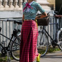 Guest wears red sunglasses, gold earrings, light green dark green pattern short sleeve shirt with hot pink bow, gold belt, dark pink hot pink green...