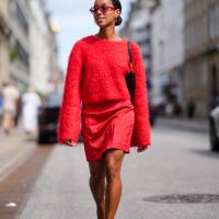 Guest wears red sunglasses, silver hoop earrings, bright red fluffy long sleeve sweater, black leather bag, bright red mini skirt, gold rings, black...