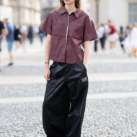 Guest wears satin wide leg trousers, a silver necklace, silver hoop earrings, black sunglasses and a burgundy short sleeved cargo shirt outside...
