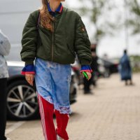 Guest wears silver earrings, a khaki nylon bomber coat, a pale blue and white tie and dye print pattern asymmetric knees dress, red with white...