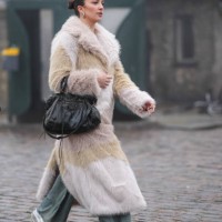 Guest wears silver earrings, a white and beige fluffy faux fur long coat, a black leather Balenciaga bag, flared pants, sneakers, outside Rolf...