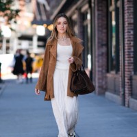 Guest wears silver layered necklaces, white pattern tank top, white flowy pants, light brown suede oversized jacket, dark brown suede bag, white...