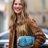 Guest wears silver necklace, black knit strapless Miu Miu top, dark brown faux fur coat, dark pink Miu Miu leather bag, outside Miu Miu, during the...