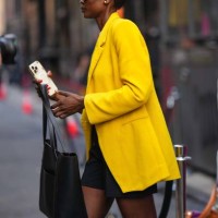 Guest wears sunglasses, a a yellow oversized blazer jacket, a skirt, a black large leather bag, holds an iphone, outside Brandon Maxwell, during New...