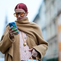 Guest wears sunglasses, a beige oversized long large fringed scarf, a matching long coat, pastel pink tweed jacket from Chanel, a blue bag from...