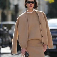 Guest wears sunglasses, a beige pastel / pale brown full look, cardigan, wool pupllover, white t-shirt, mini skirt, a white mini bag, outside Miu...