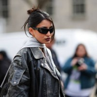 Guest wears sunglasses, a gray scarf, a black oversized biker leather jacket , a black t-shirt , black underwear on top of black tights, outside...