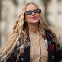 Guest wears sunglasses, a long beige wool cardigan, a gray black and red long jacket, outside Chanel, during the Womenswear Spring/Summer 2024 as...
