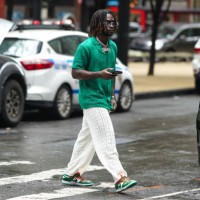 Guest wears sunglasses, a necklace a green shirt, white pants with floral embroidery, Nike green sneakers, outside Jason Wu, during New York Fashion...