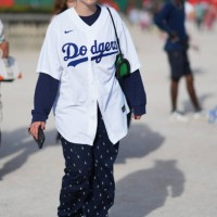 Guest wears sunglasses, a Nike baseball Dodgers shirt, a blue pulllover, navy blue flowing pants with printed details, sneakers, outside Casablanca,...