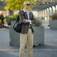 Guest wears sunglasses, a pale blue shirt, a checkered blazer jacket, a black leather bag, a belt, beige pants, black leather shoes, outside COS,...