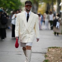 Guest wears sunglasses, a white shirt, a tie, a cream color oversized blazer jacket, white shorts, knee high boots, outside Giambattista Valli,...