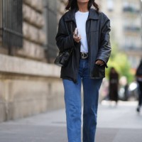 Guest wears sunglasses, a white top, a black leather jacket, a belt, blue jeans, outside Hermes, during the Womenswear Spring/Summer 2024 as part of...
