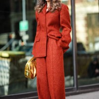 Guest wears sunglasses, an orange oversized blazer jacket with shoulder pads, cotton pants , a golden shiny bag, outside Carolina Herrera, during New...