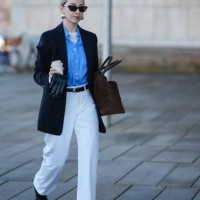 Guest wears sunglasses, earrings, a blue shirt, a white top, a black oversized blazer jacket , a belt, white pants , pointed black leather shoes, a...