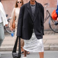 Guest wears sunglasses, earrings, a necklace, a gray t-shirt, a black oversized blazer jacket, a silver shiny sequined midi skirt, New Balance...