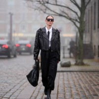 Guest wears sunglasses, earrings, a white shirt, a black tie, a black leather jacket with texture and details, a midi black skirt, a woven leather...