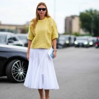 Guest wears sunglasses, earrings, a yellow knit pullover, a white godet midi skirt, brown suede pointy mules, outside Prada, during the Milan Fashion...