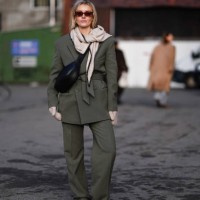 Guest wears sunglasses , golden earrings, a gray scarf, a green khaki oversized blazer jacket , a black leather bag, suit flared pants , sneakers...