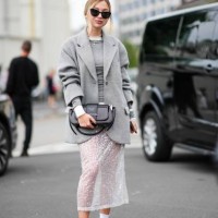 Guest wears sunglasses, necklaces, a grey pullover, a grey fluffy jacket, a two-tone Prada bag, a sequined white transparent lace midi skirt, white...