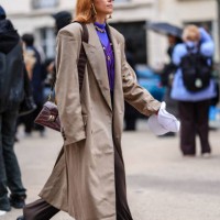 Guest wears transparent glasses, gold earrings, bright purple long sleeve shirt, dark purple v-neck sweater with gold detail, dark brown blazer...