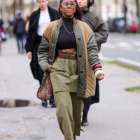 Guest wears transparent glasses, silver hoop earrings, black turtleneck long sleeve cropped shirt, silver chain necklace, dark green high waisted...