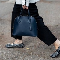 Guest wears white jacket, black skirt, Alaia shoes, navy bag outside Ferragamo during the Milan Fashion Week Menswear Spring/Summer 2025 on September...