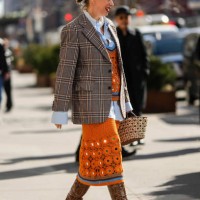 Guest wears white pearls earrings, a white embroidered pearls large necklace, a pale blue shirt, an orange wool cut-out pattern with brown and blue...