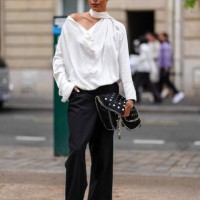 Guest wears white satin long sleeve half shoulder shirt, black loose pants, black Stella McCartney leather bag with silver detail, outside Stella...