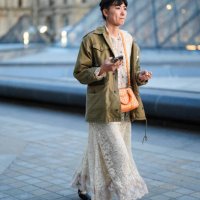 Guest wears white sheer mesh lace midi dress, bright orange bag, dark green oversized jacket, white socks, black ballerina flats leather shoes,...