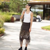 Guest wears white tank top, black skirt, black socks, black sneakers, green bag with fur and sunglasses outside the Marimekko show during day four of...