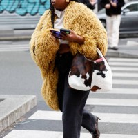 Guest wears yellow fur jacket, white cropped shirt, black jeans, brown boots, cow print bag, outside Junya Watanabe, during the Menswear Fall Winter...