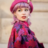 Guest with pink hair is seen wearing red, pink, purple and black flower pattern jacket, matching color checkered skirt, pink beret and pink bag...