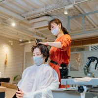 hair dresser drying costumer's hair. owner and customer wearing protective face mask for illness prevention - hairstyle stock pictures, royalty-free photos & images