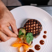 hand of a chef garnishing a fillet of beef with herbs and vegetables on a ceramic plate in a kitchen - food stock pictures, royalty-free photos & images