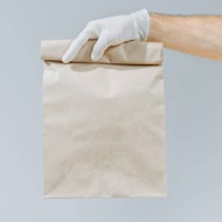 hand of a man in a glove holding a brown bag or bag for taking out isolated on a gray background. packaging layout template. delivery service concept. copy space. courier - junk food stock pictures, royalty-free photos & imag