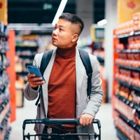 handsome asian male searching for groceries from the list on his mobile phone - food stock pictures, royalty-free photos & images