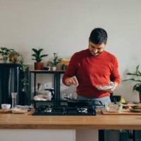 handsome cheerful man standing in a kitchen preparing a meal - food stock pictures, royalty-free photos & images
