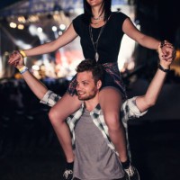 handsome guy holding a cute girl friend on his shoulders. stage glowing in the bakcground - concert stock pictures, royalty-free photos & images
