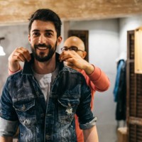 handsome man trying on new denim jacket with stylist in modern boutique - fashion stock pictures, royalty-free photos & images