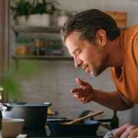 handsome young man enjoying the aroma of a meal in a kitchen - food stock pictures, royalty-free photos & images