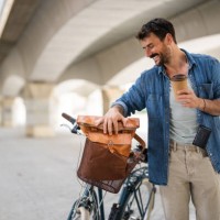 handsome young man with bicycle in a city and takeaway cup of coffee - junk food stock pictures, royalty-free photos & images
