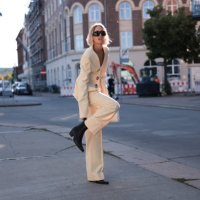 Hannah Stefansson is seen wearing black sunglasses, a light yellow suit, a white leather bag, and pointed black Chelsea boots from Copenhagen Studios...