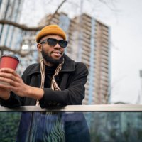happy american guy holding take away coffee and looking into distance while walking in urban area - coffee stock pictures, royalty-free photos & images