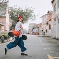 happy asian chinese young woman crossing road carrying skateboard in old town - travel stock pictures, royalty-free photos & images