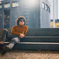 happy asian malay young man looking away sitting on ground with backlit sunlight in city street - fashion stock pictures, royalty-free photos & images