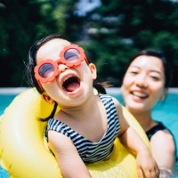 happy asian toddler girl with sunglasses smiling joyfully and enjoying family bonding time with mother having fun in the swimming pool in summer - travel stock-fotos und bilder