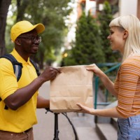 happy black courier handing over a delivery to his female customer. - junk food stock pictures, royalty-free photos & images