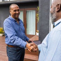 happy businessman shaking hands with male customer while standing outside house - home decoration stock pictures, royalty-free photos & images